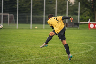 man in yellow and black soccer jersey kicking soccer ball on green grass field during daytime