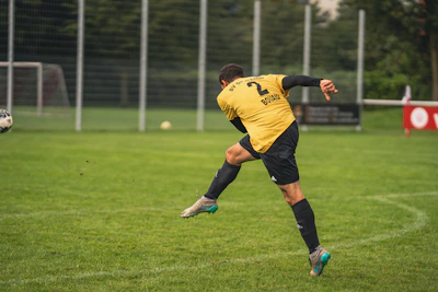 man in yellow and black soccer jersey kicking soccer ball on green grass field during daytime