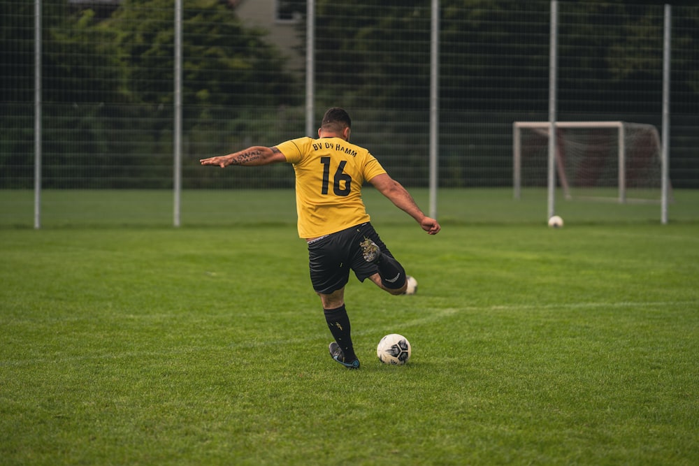 Mann im gelb-schwarzen Fußballtrikot kickt tagsüber Fußball auf grünem Rasen