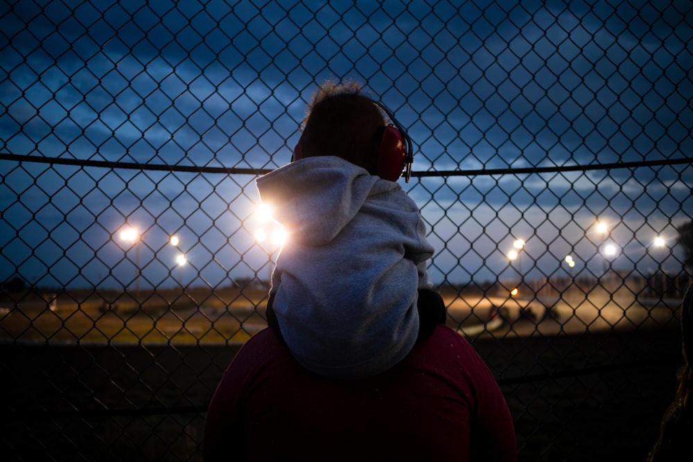 homme en sweat à capuche blanc debout près de la clôture pendant le coucher du soleil