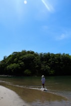 A cheerful person wearing shorts and walking along a sunny beach path.