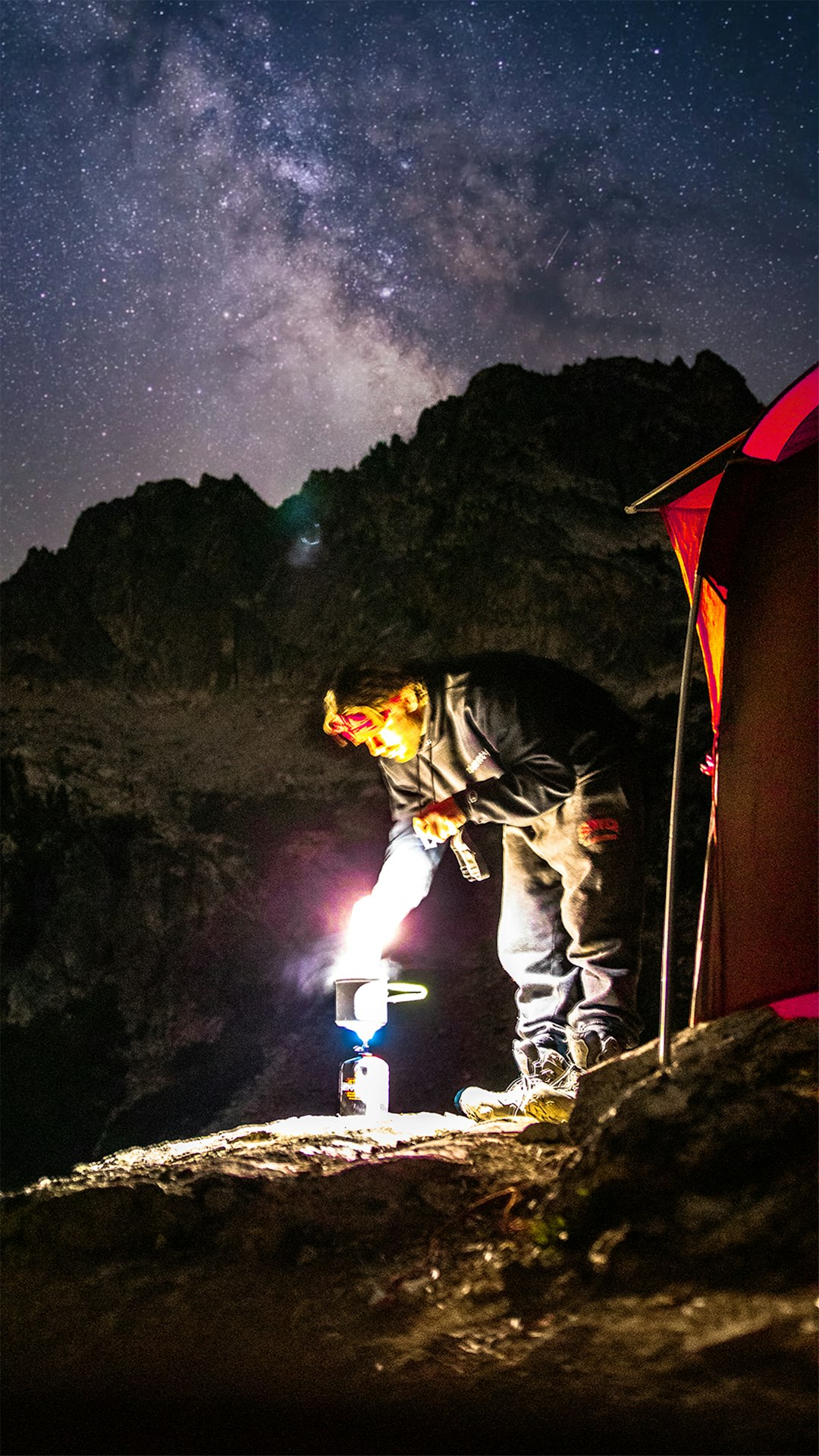 man in black jacket and white pants standing beside red tent during night time