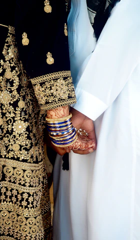 A mother and daughter holding hands, both wearing matching cultural outfits with intricate patterns.
