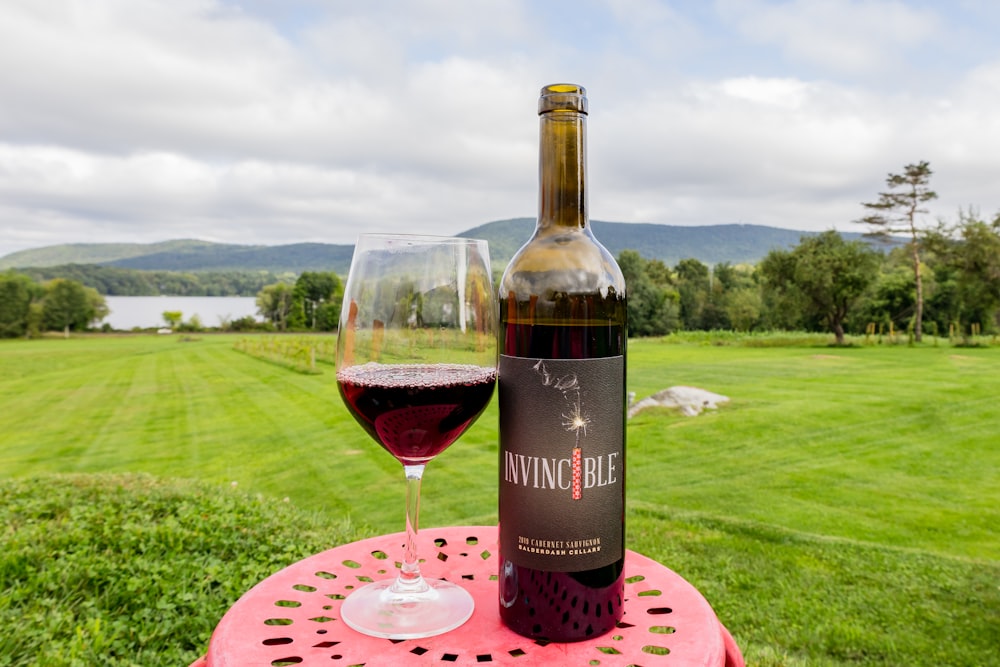 black and red labeled bottle beside wine glass on pink table mat