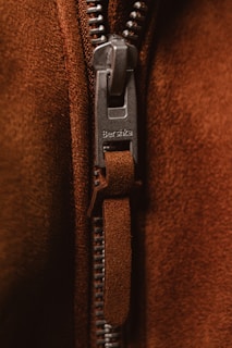 Detail of a branded zipper pull on a stylish streetwear jacket against a concrete wall