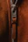 Close-up view of a zipper pull on a brown suede fabric, with the brand name visible on the metallic part of the zipper.