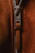 Close-up view of a zipper pull on a brown suede fabric, with the brand name visible on the metallic part of the zipper.