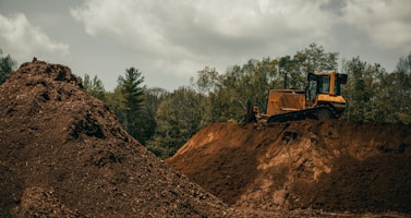 yellow and black heavy equipment on brown rocky hill under white cloudy sky during daytime