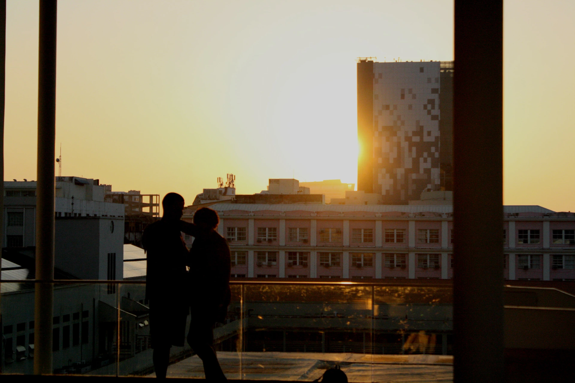 The couple relaxing on a small balcony, enjoying a quiet moment with coffee and city views at sunset.
