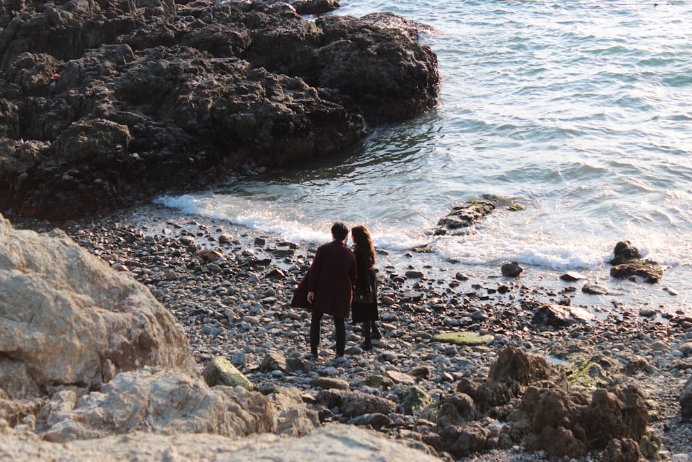 2 person standing on rocky shore during daytime