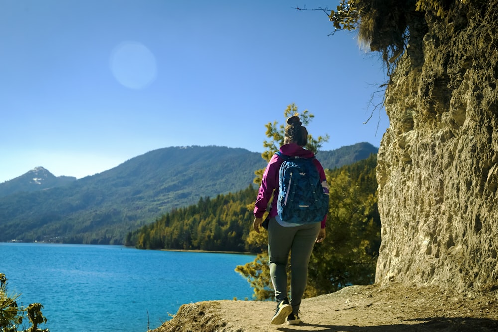 man in red and black jacket standing on rock near body of water during daytime