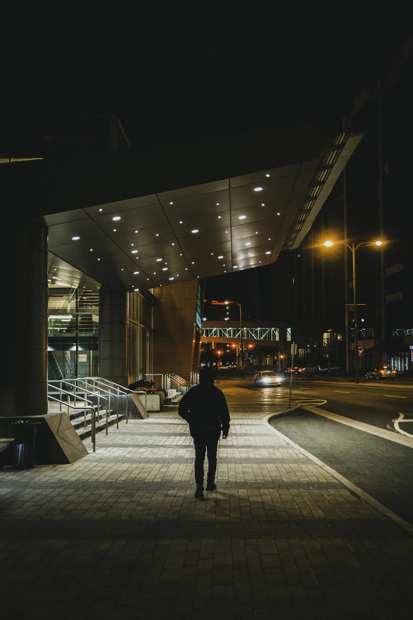 man in black jacket walking on sidewalk during night time