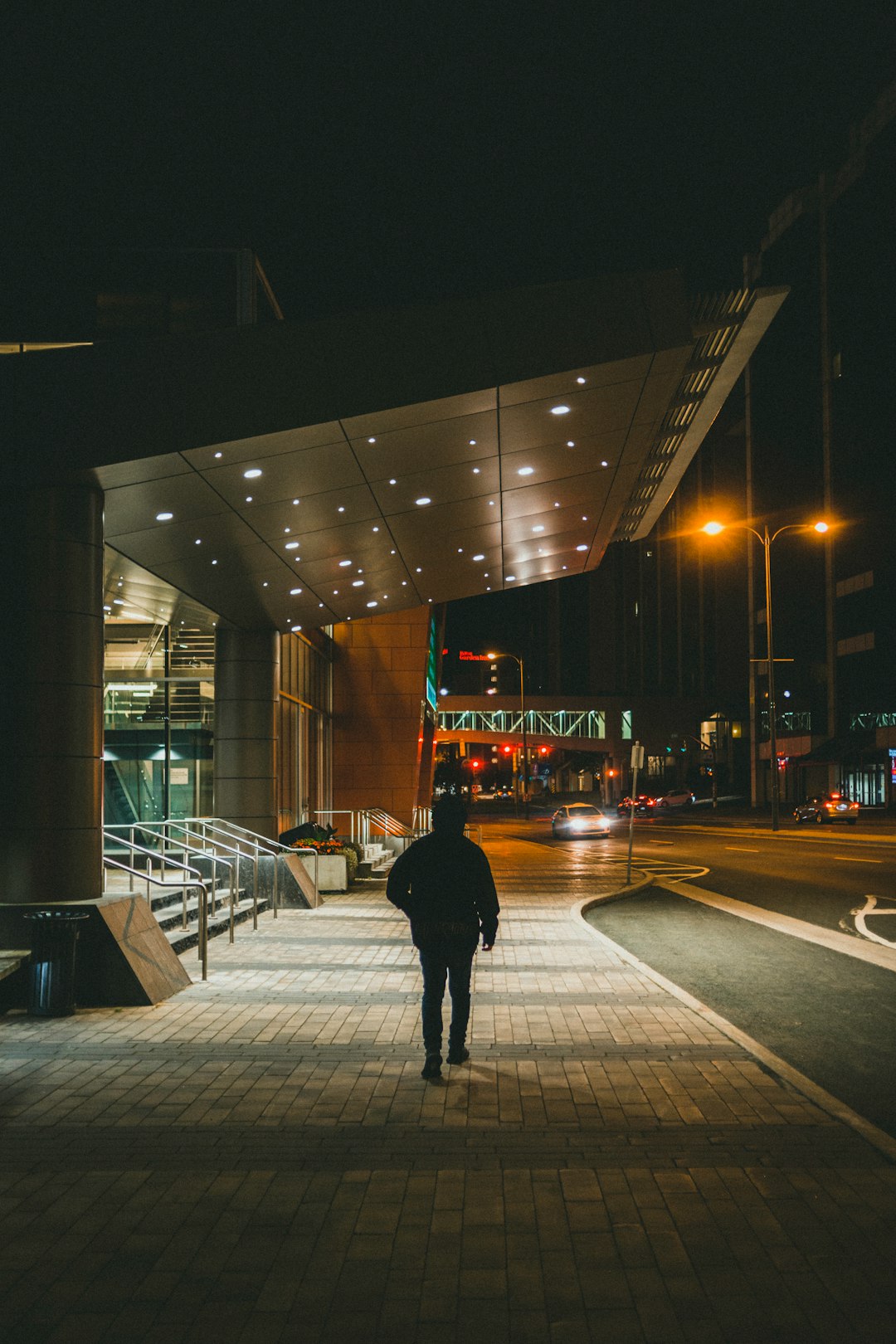 man in black jacket walking on sidewalk during night time