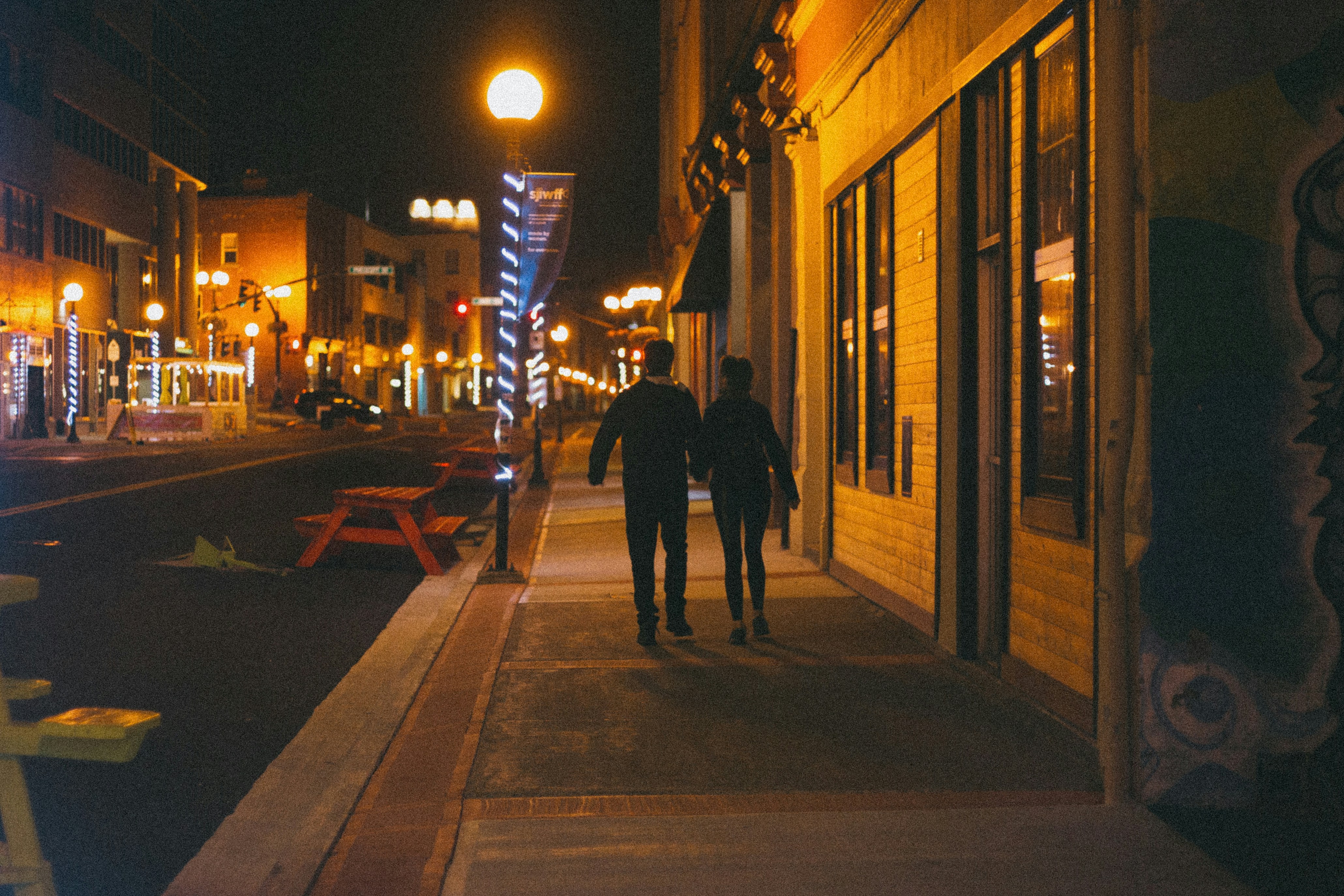 man in black jacket walking on sidewalk during night time