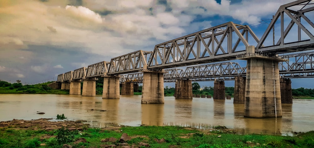 gray concrete bridge over river under cloudy sky during daytime