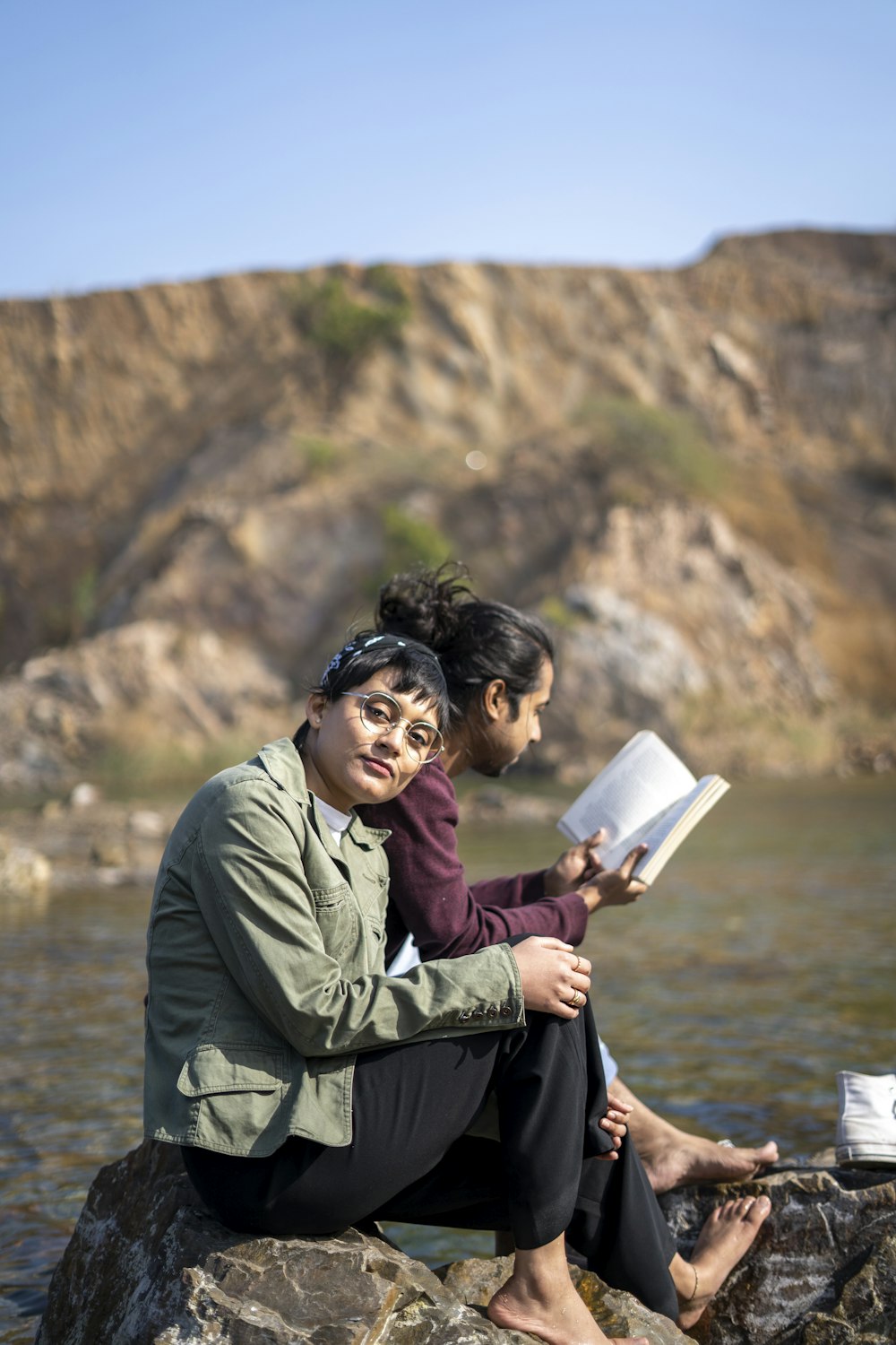 man in green jacket sitting on rock reading book