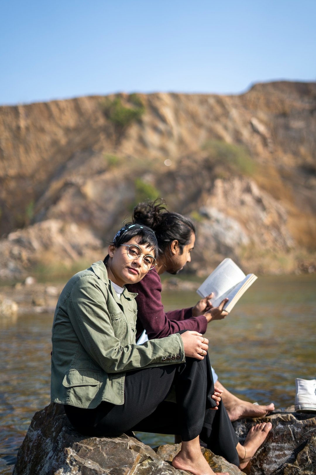 man in green jacket sitting on rock reading book