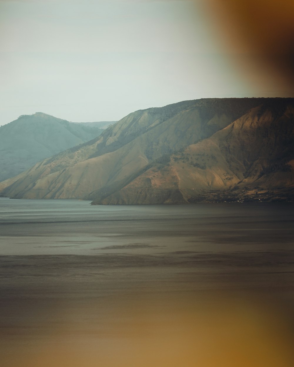 brown mountain beside body of water during daytime