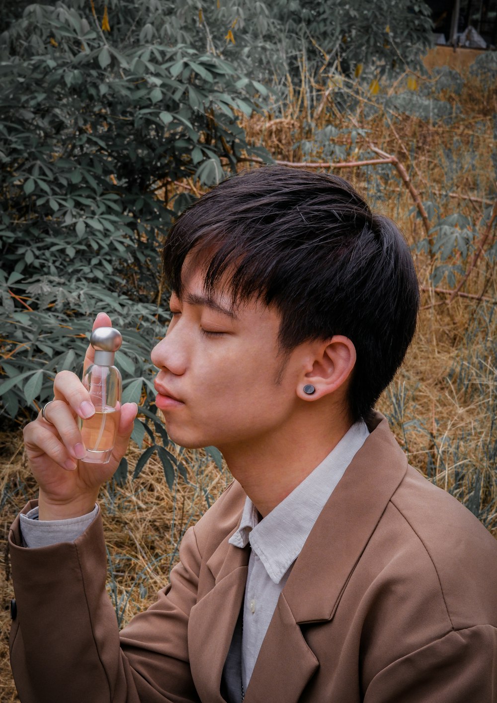 man in brown blazer holding clear glass bottle