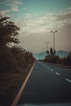 gray concrete road between green trees under white clouds and blue sky during daytime