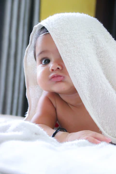 A baby with a black bracelet under a white towel on a bed