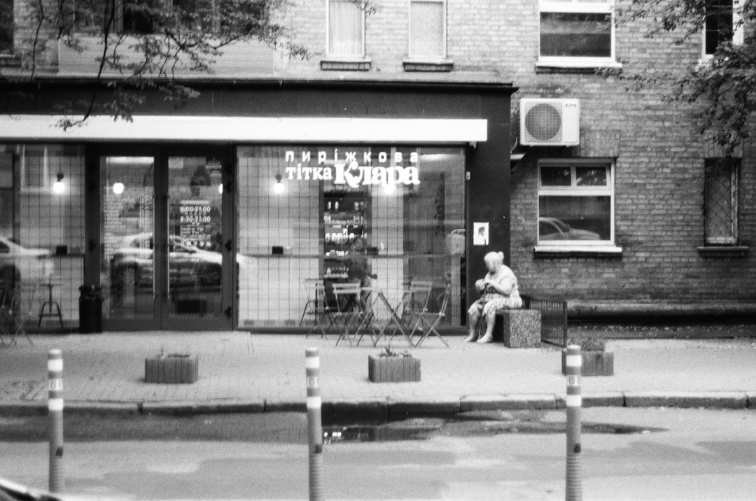 grayscale photo of 2 women sitting on bench near building