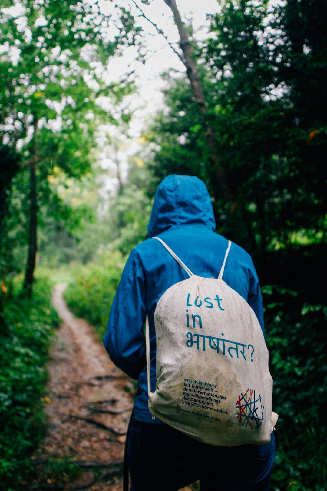 person in blue and white hoodie standing on brown dirt road in forest during daytime