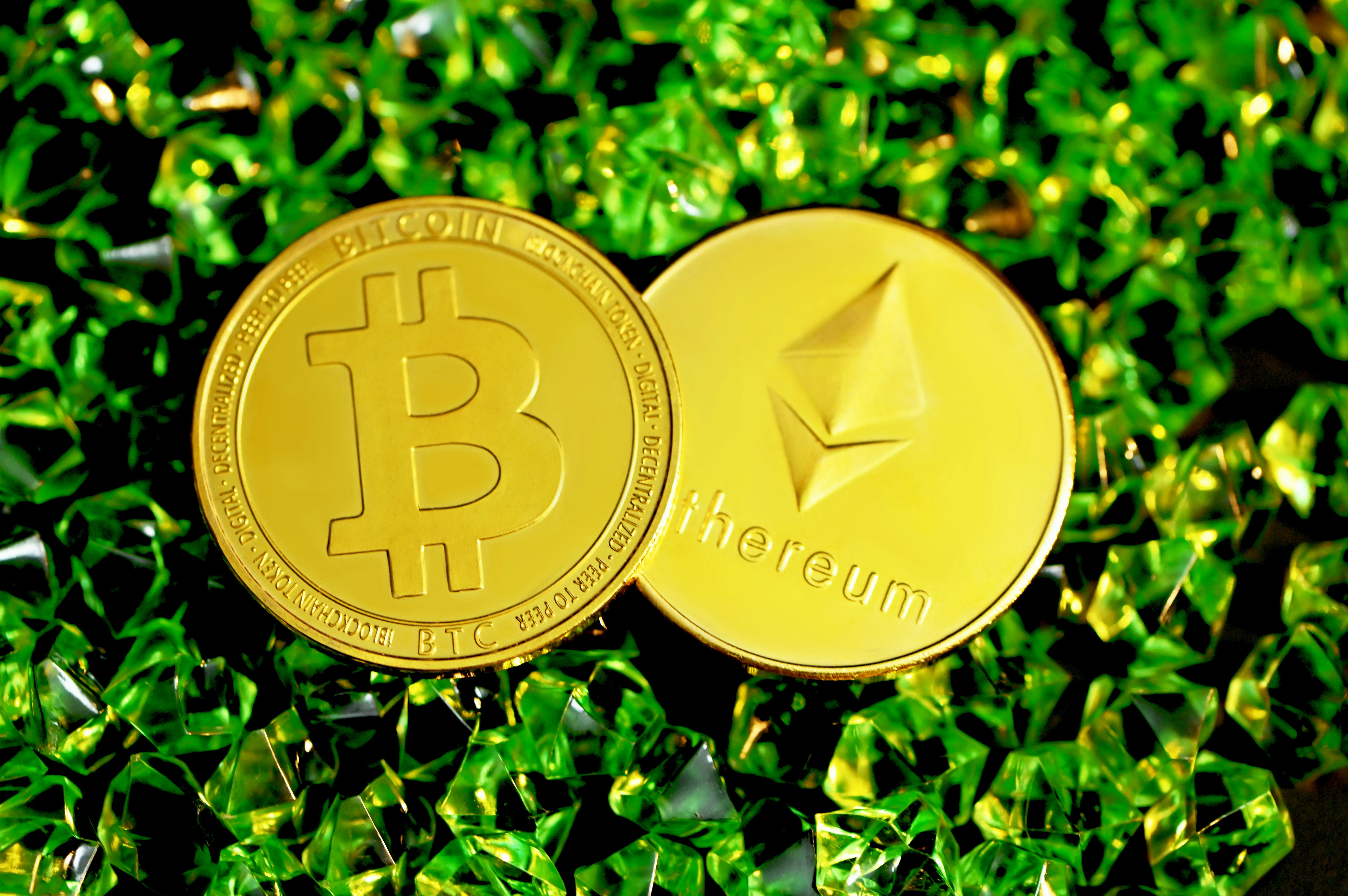 A Bitcoin and an Ethereum coin are together on the green crystals