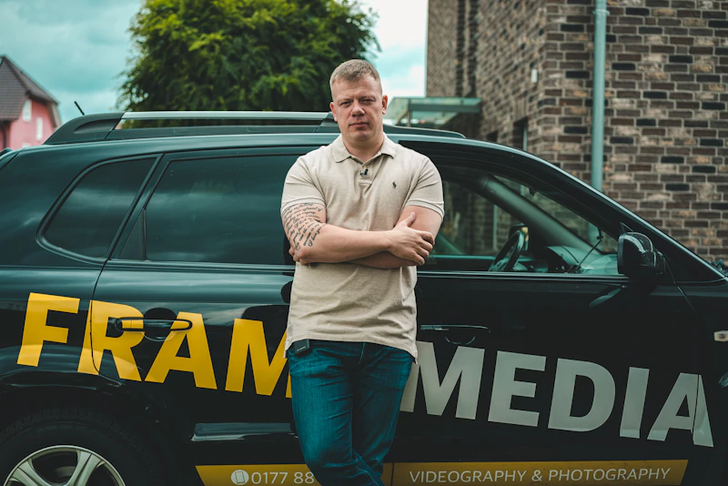 Man in gray long sleeve shirt and blue denim jeans standing beside blue and yellow car