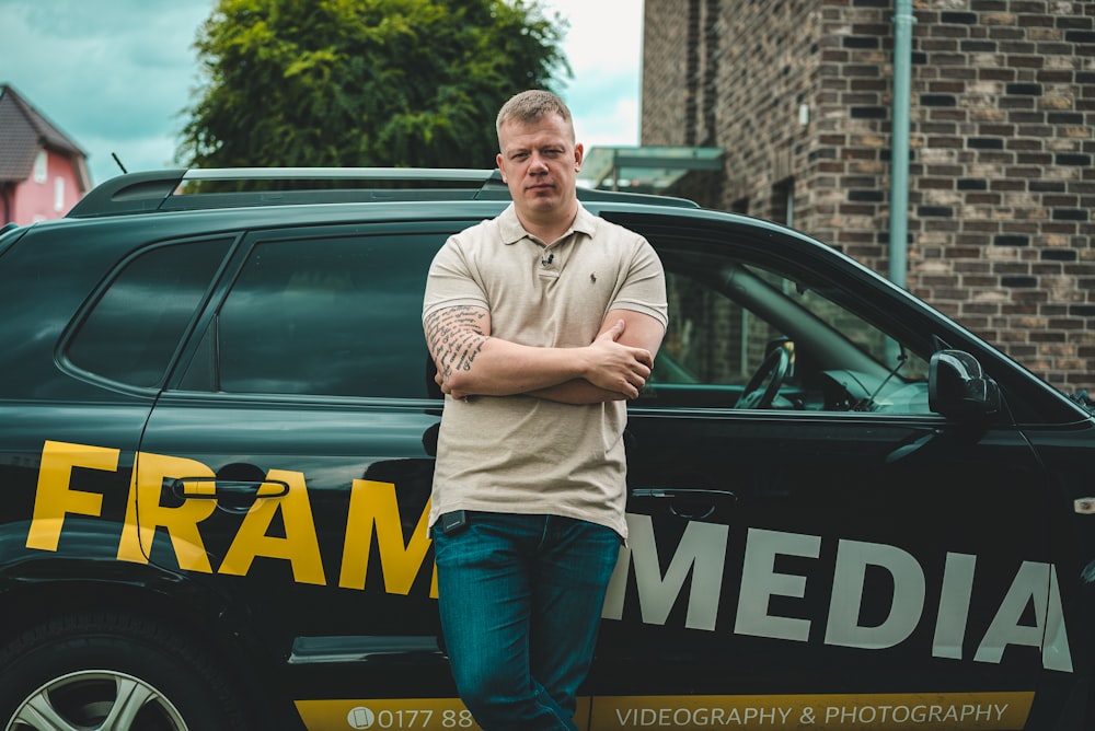 man in gray long sleeve shirt and blue denim jeans standing beside blue and yellow car