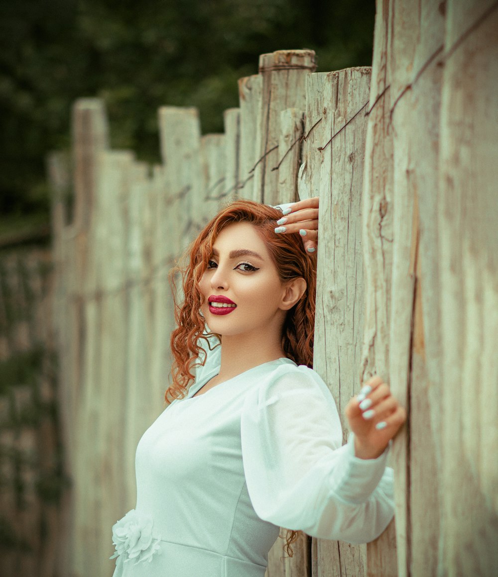 woman in white long sleeve dress leaning on brown wooden fence during daytime