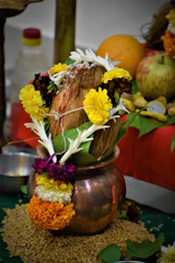 A shiny brass kalash filled with water and decorated with fresh flowers in a traditional pooja space.