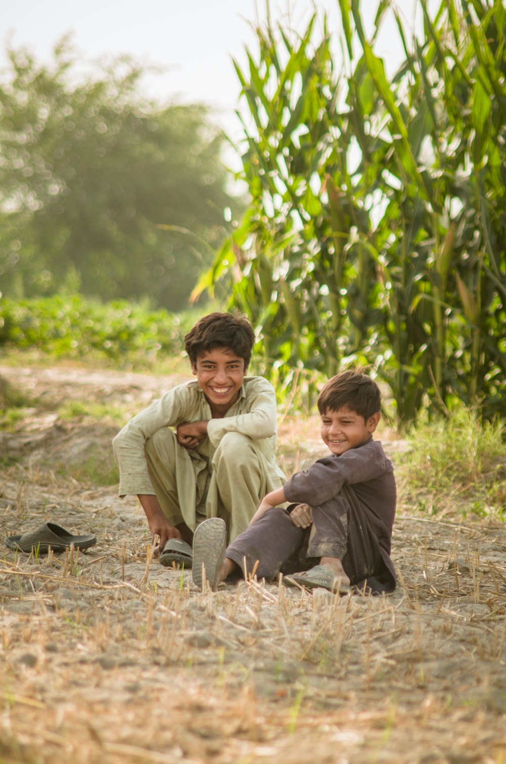 2 boys sitting on ground near corn plant during daytime