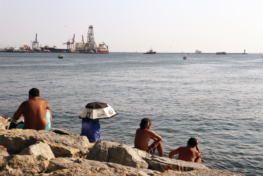 people sitting on rock near sea during daytime