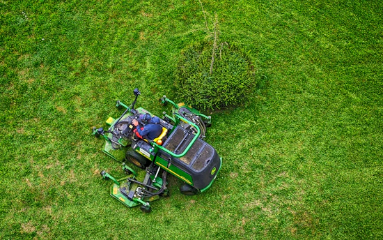 A cheerful gardener adjusting a sleek robotic lawn mower in a lush Bayonne garden.