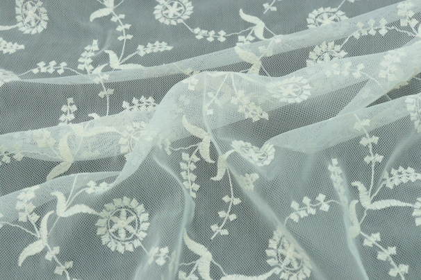 Soft ivory organza saree with delicate floral embroidery, flowing gracefully against a minimalist beige backdrop.
