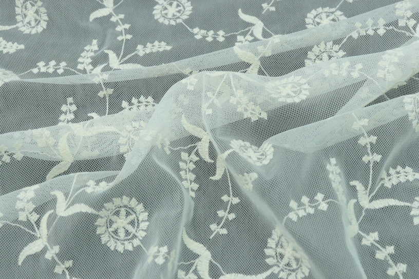 Close-up of delicate floral embroidery on sheer tulle fabric in soft ivory.