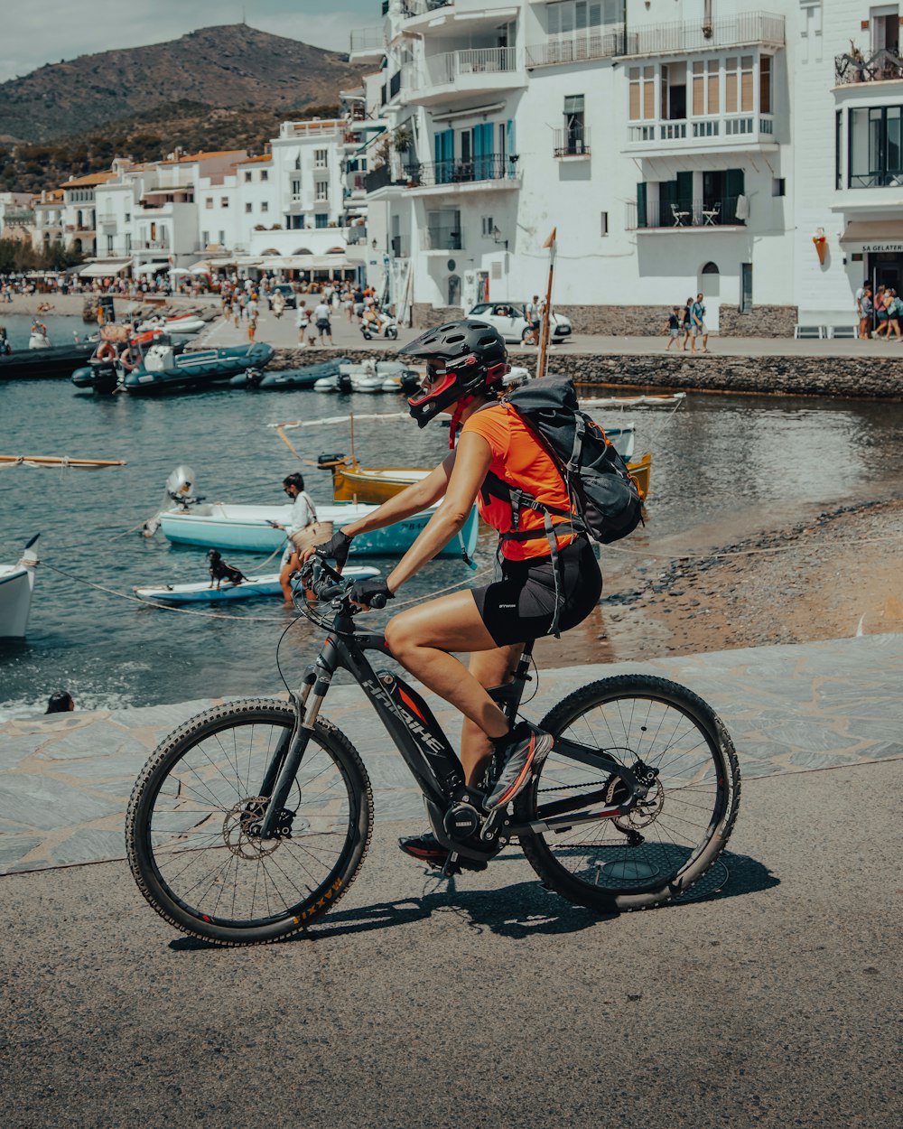 woman in black and orange shirt riding on bicycle near body of water during daytime