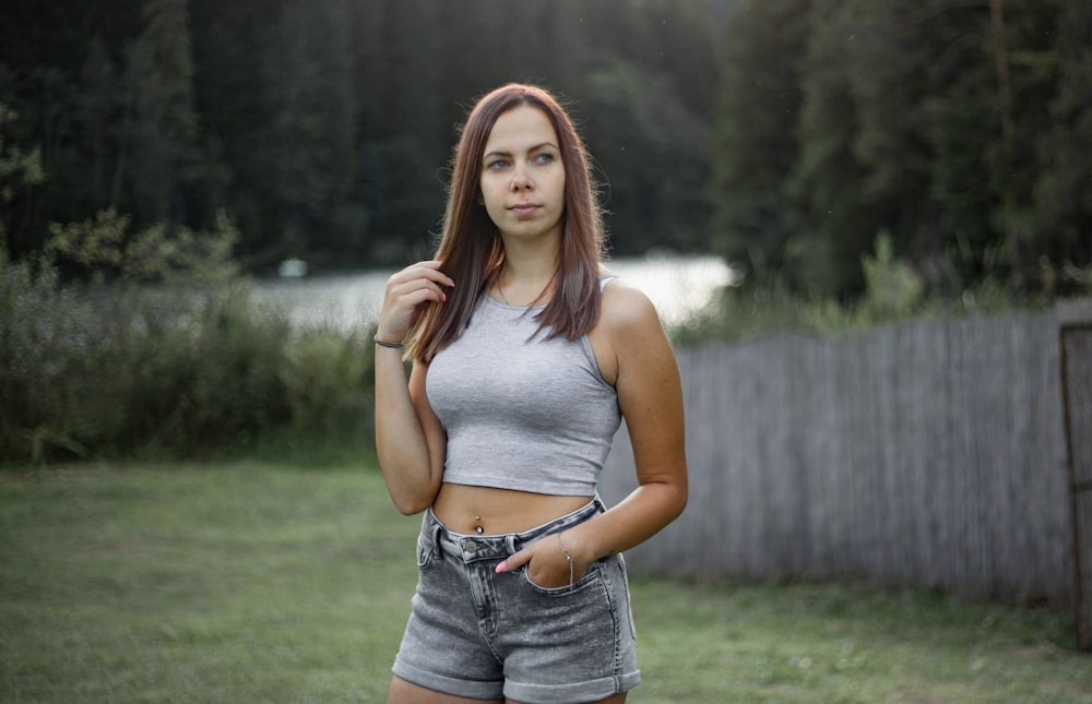 woman in gray tank top and blue denim shorts standing on green grass field during daytime