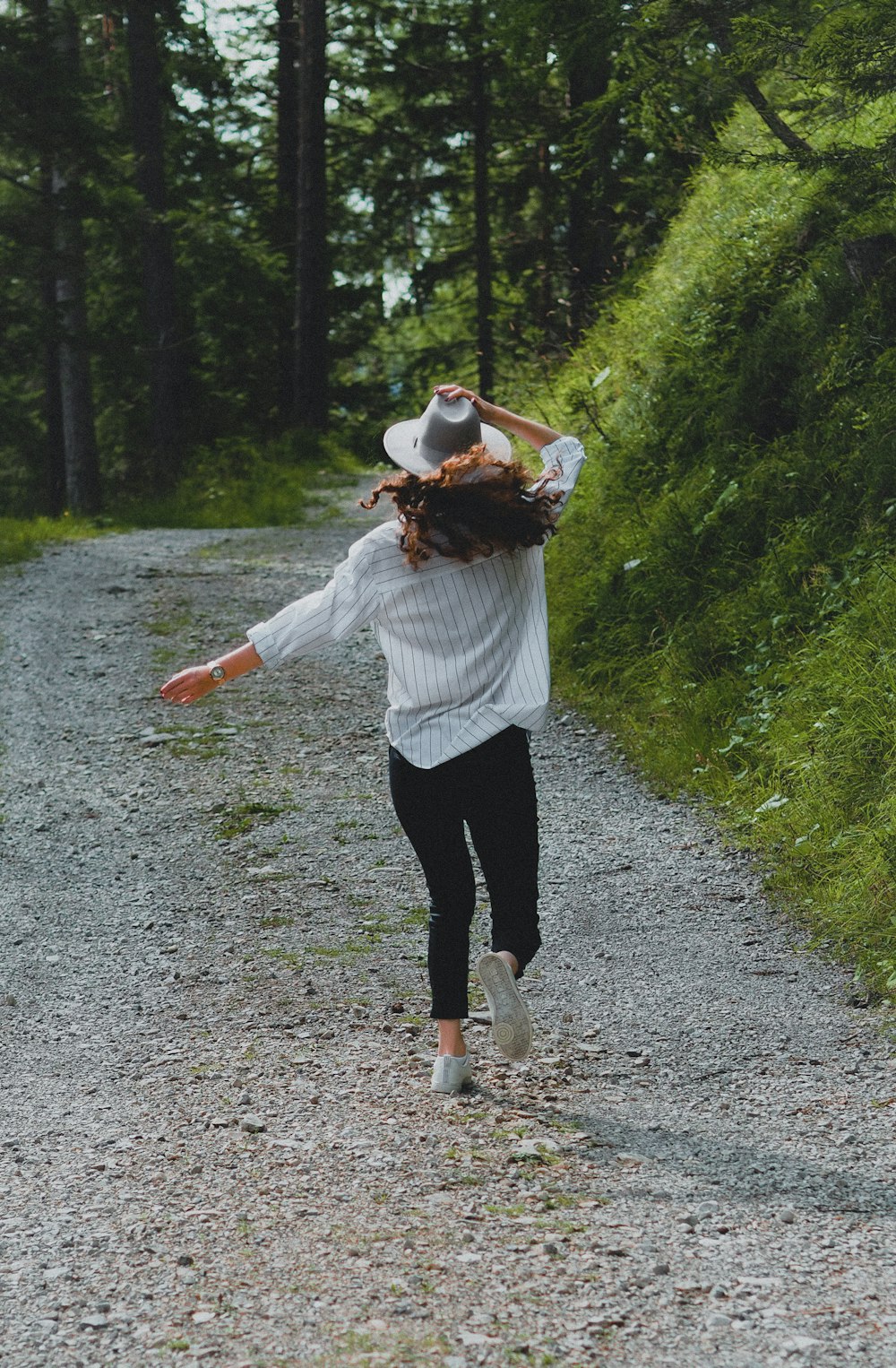 Mujer con camisa blanca de manga larga y pantalones negros caminando por camino de tierra durante el día
