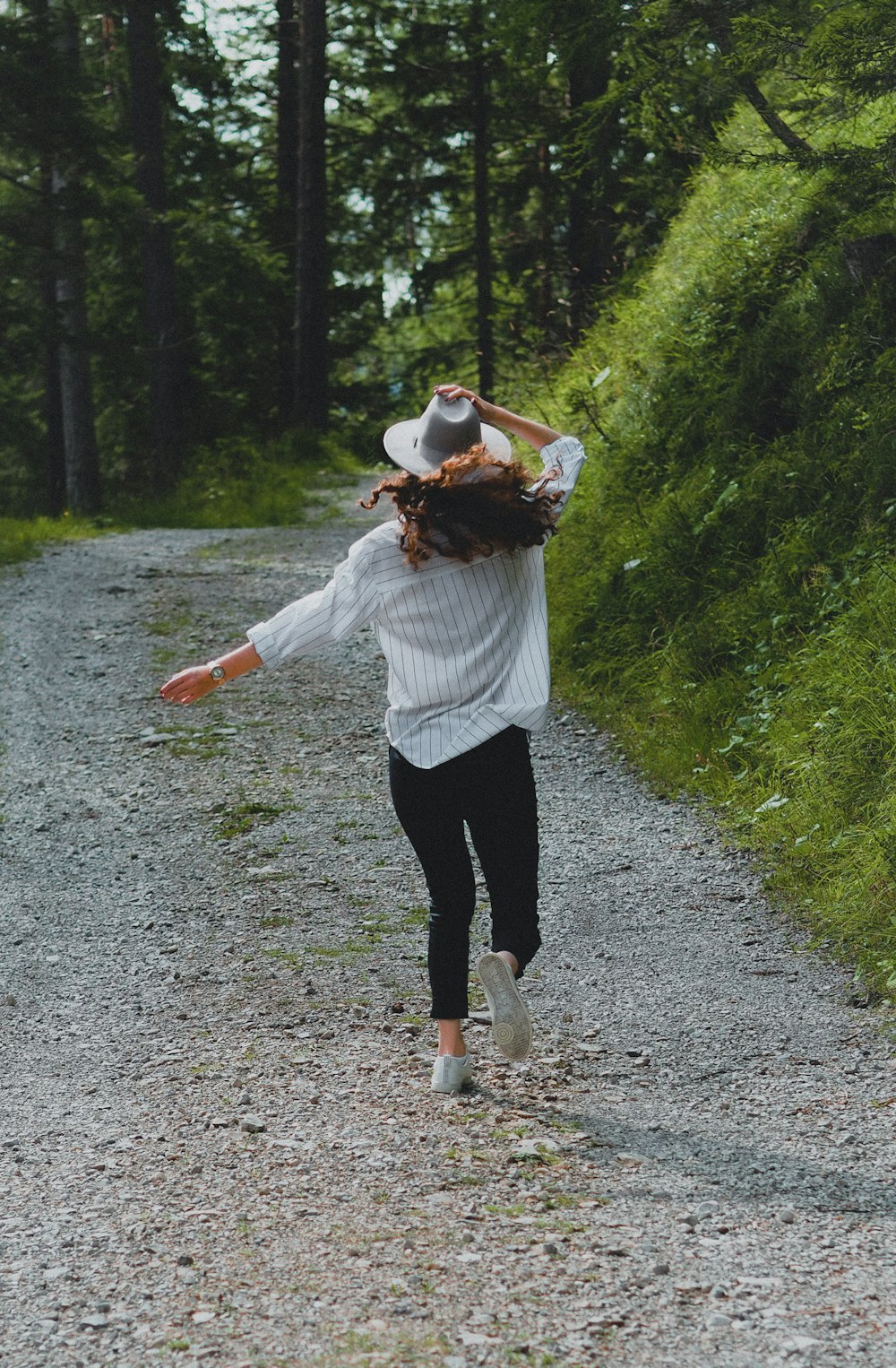 woman in white long sleeve shirt and black pants walking on dirt road during daytime