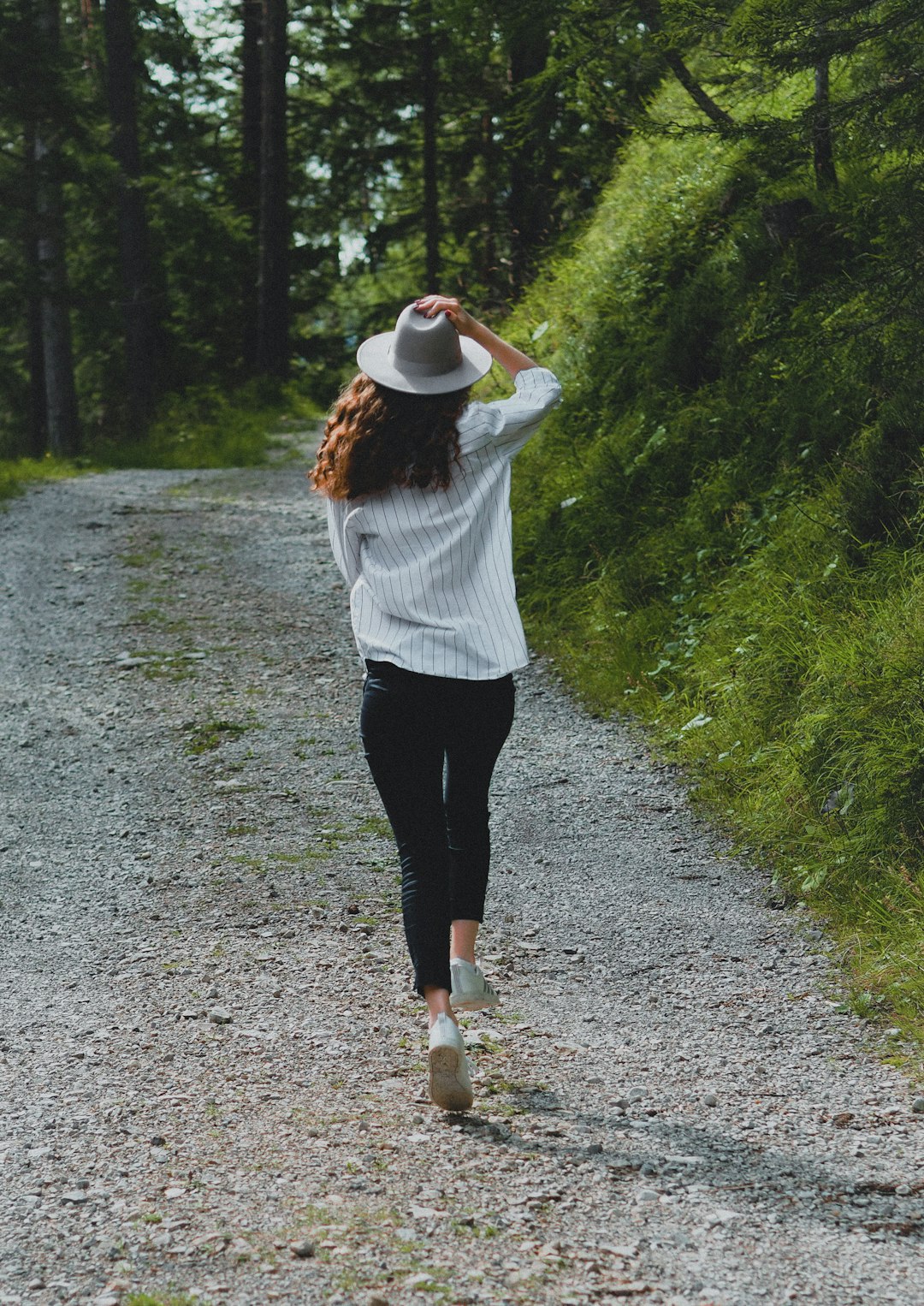woman in white long sleeve shirt and black pants walking on dirt road during daytime
