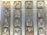 A collection of stone relief sculptures displayed within a glass case. Each relief depicts a human figure, mostly in regal or attentive postures. The sculptures appear to be ancient, with detailed carvings emphasizing clothing folds and facial features.