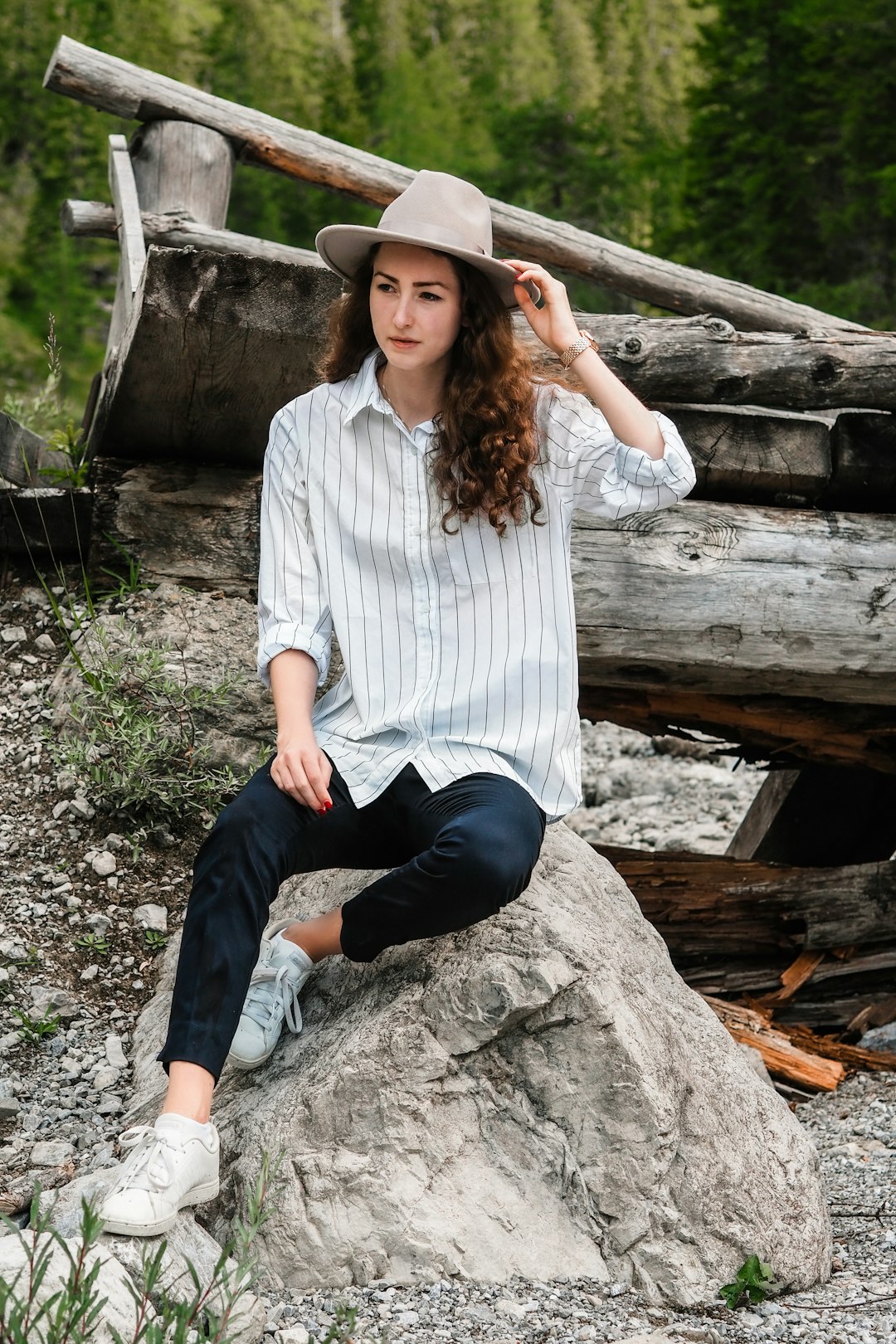 woman in white and blue striped button up shirt and black pants sitting on gray rock