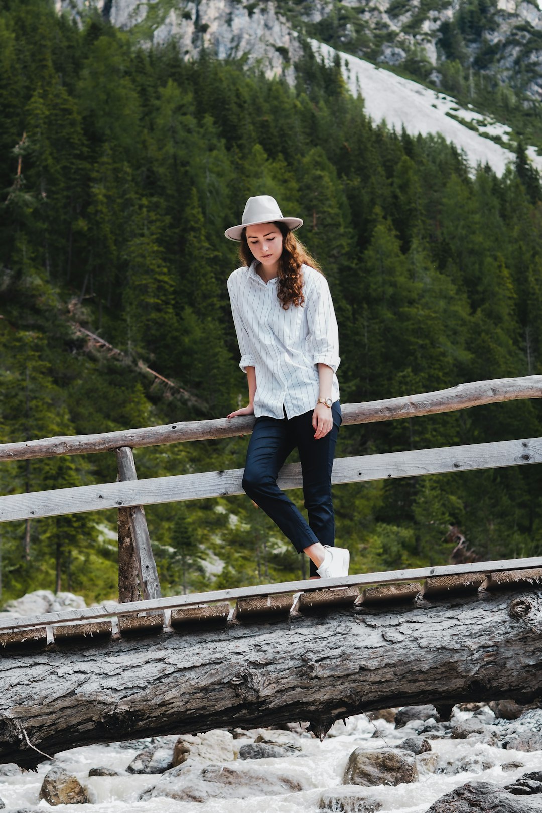 man in white dress shirt and blue denim jeans standing on wooden bridge during daytime