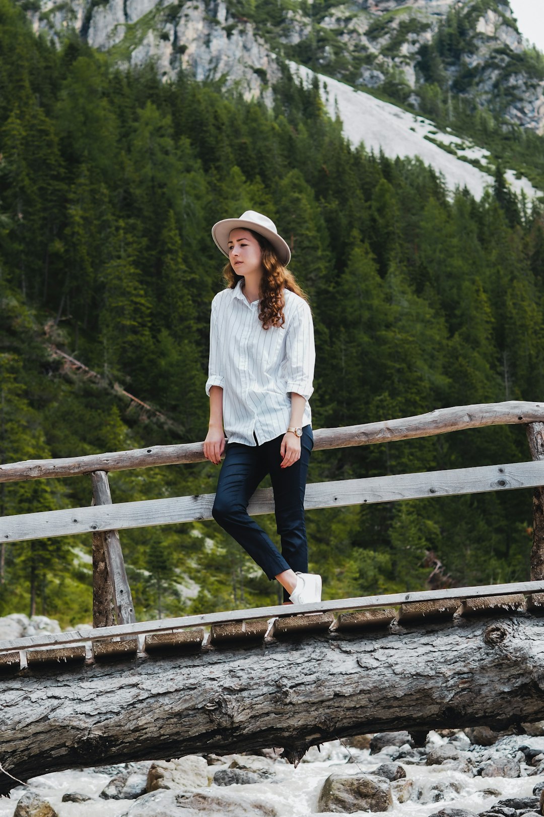 woman in white dress shirt and blue denim jeans standing on wooden bridge during daytime