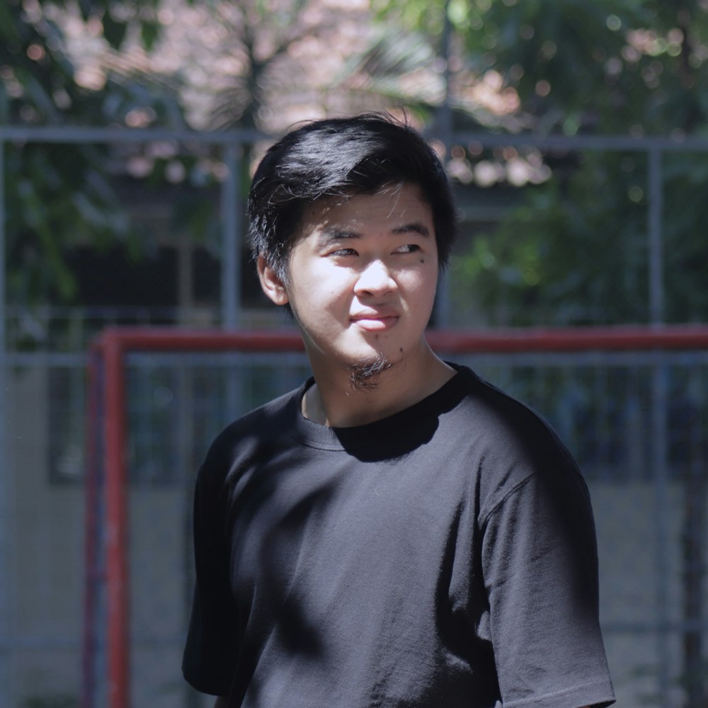 man in black crew neck shirt standing near red metal fence during daytime