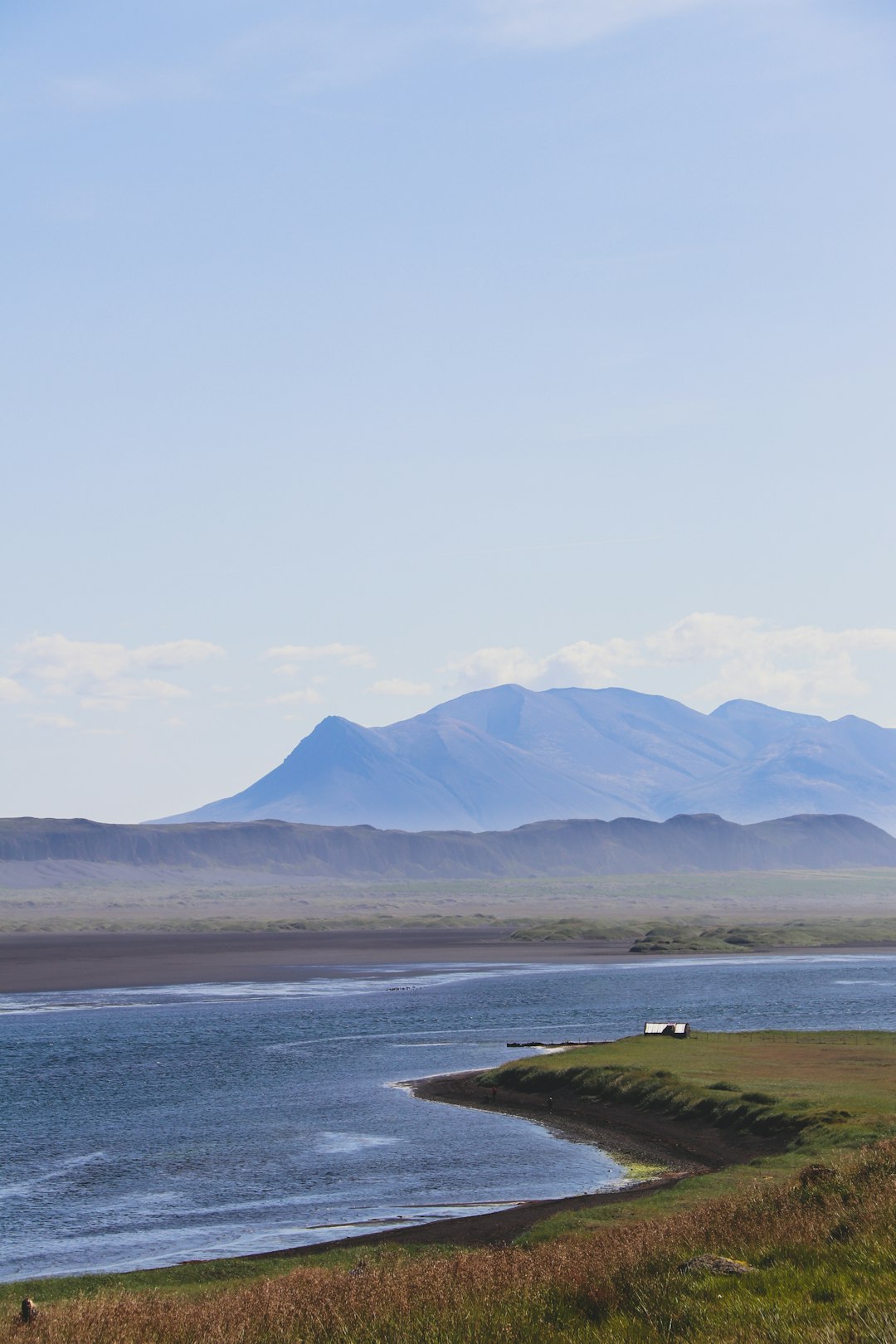 green grass field near body of water and mountains during daytime