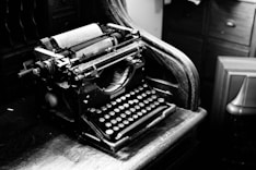 A dimly lit vintage typewriter on a dark wooden desk, with scattered pages and a faint glow highlighting the keys.