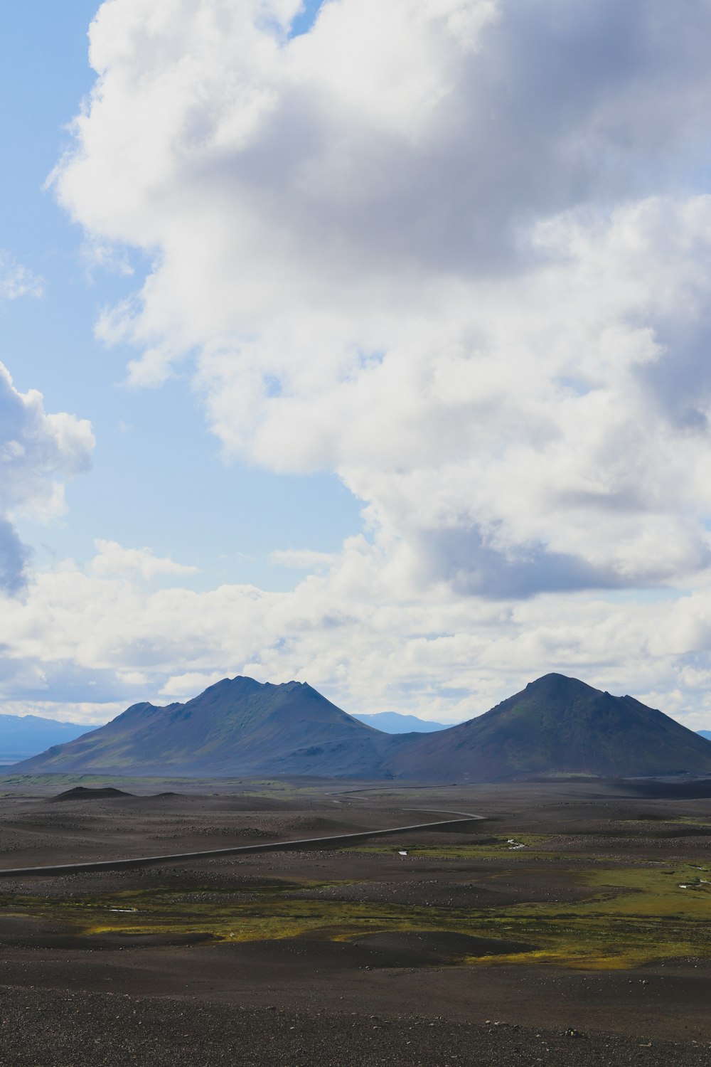 green grass field near mountain under white clouds during daytime